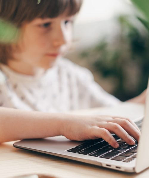 Distance learning online education. Caucasian smile kid boy studying at home with laptop and doing school homework. Thinking child siting at table with notebook. Back to school.