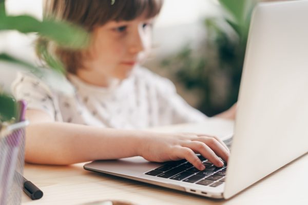 Distance learning online education. Caucasian smile kid boy studying at home with laptop and doing school homework. Thinking child siting at table with notebook. Back to school.